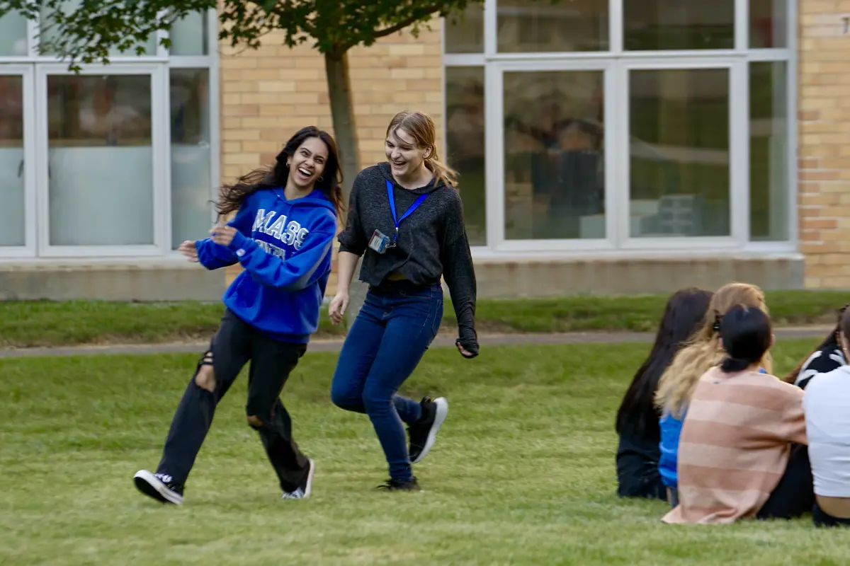 Two college age girls are frolicking as one apparently chases the other on a grass field