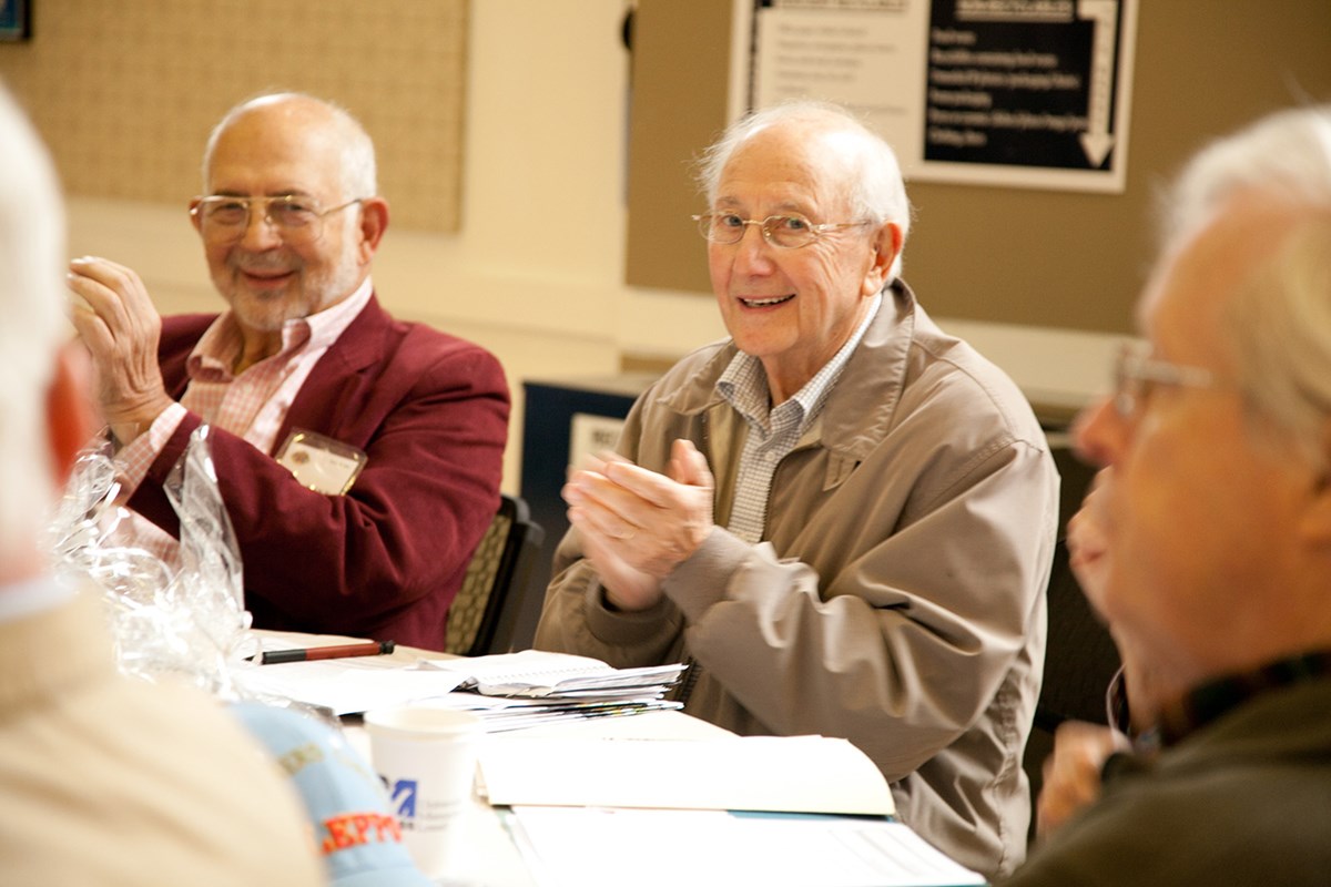 Two elderly or older men sitting at a table clapping during a Learning in Retirement event.