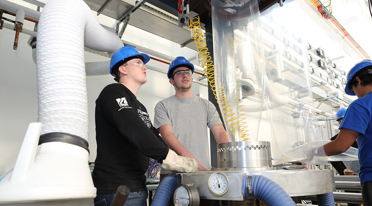 Two male UMass Lowell students wearing hard hats while working in a Plastics recycling lab.