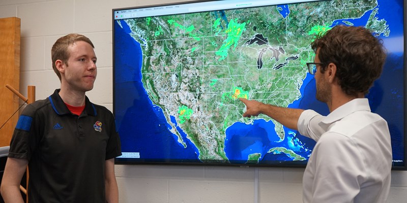 Christopher Skinner points at a weather map on a screen with Tyler Harrison looking on