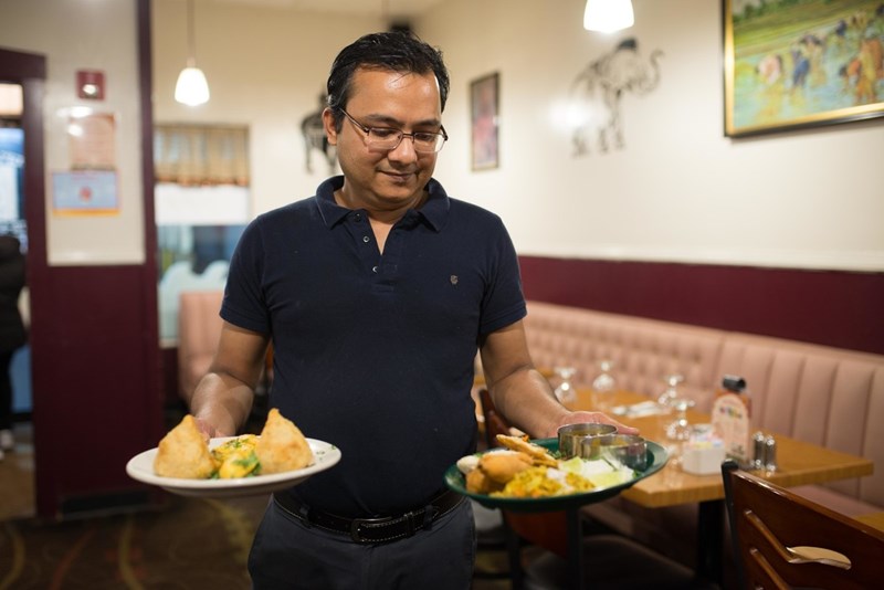 A man carries samosas and other Indian food to a table at Udupi Bhavan in Lowell, MA