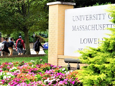 Granit sign with University of Massachusetts Lowell and students walking on sidewalk.