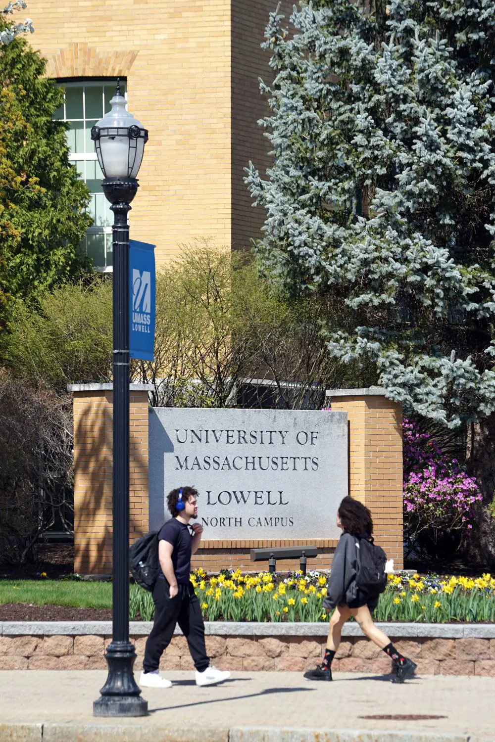 Two students walk past UMass Lowell North Campus sign on sidewalk