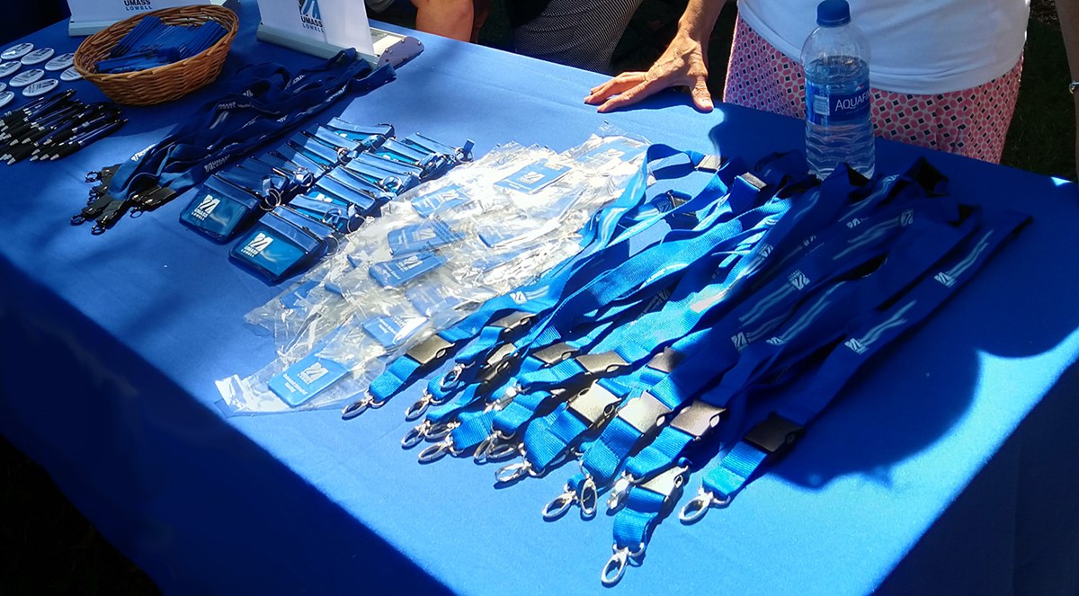A table displaying UMass Lowell branded swag including: lanyards, wallets, pens, pins and more.