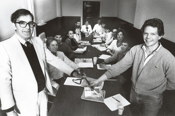 Black and white shot of history Prof. Dean Bergeron, who advised the Model U.N. team for many years, with student Brian Kenny '87, holding a gavel in front of a boardroom table of seated students