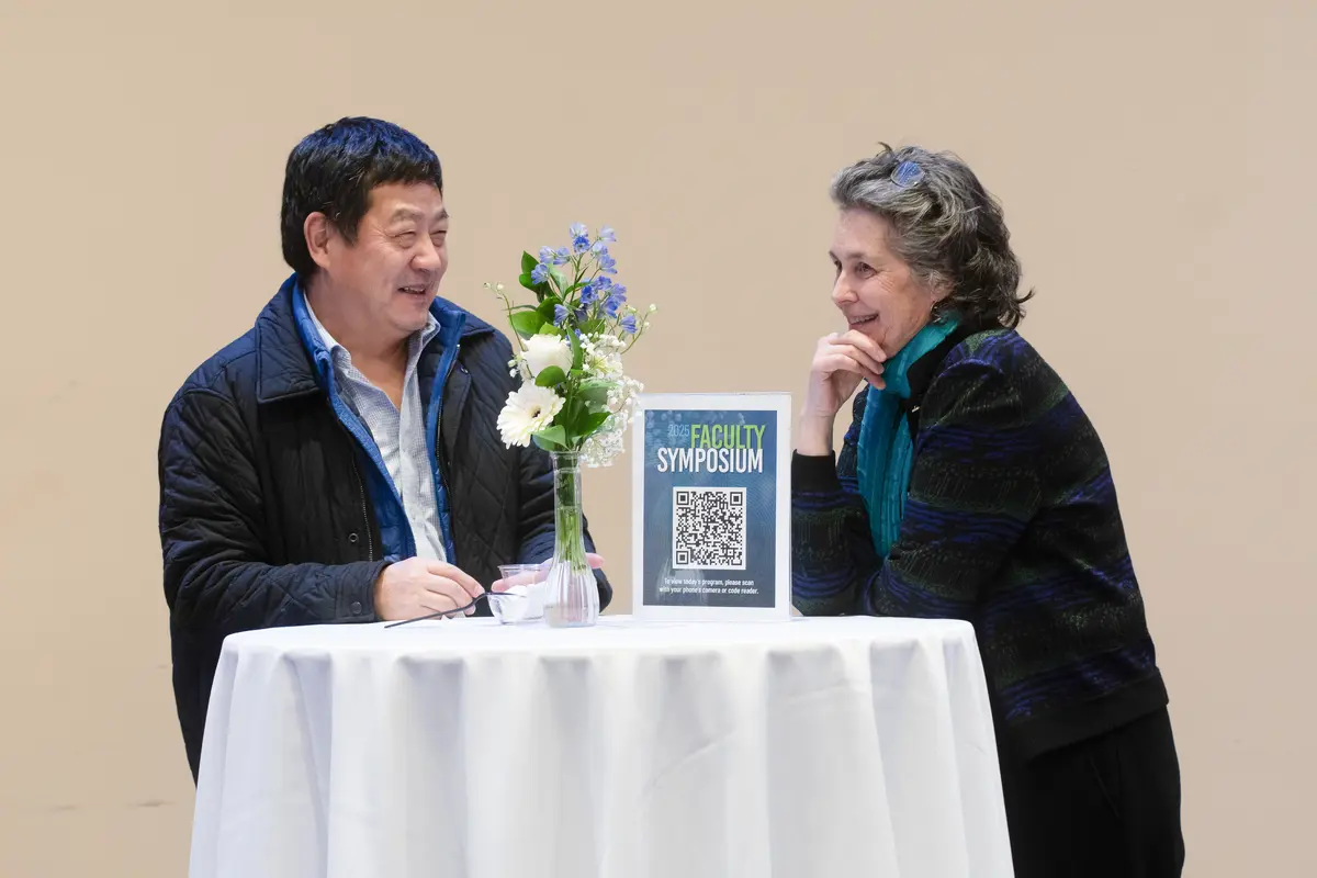 Two faculty members smiling in a conversation.