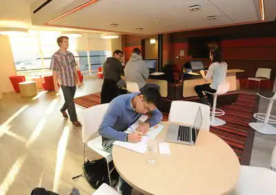 Students work at tables and at bars in sunny common area at University Suites