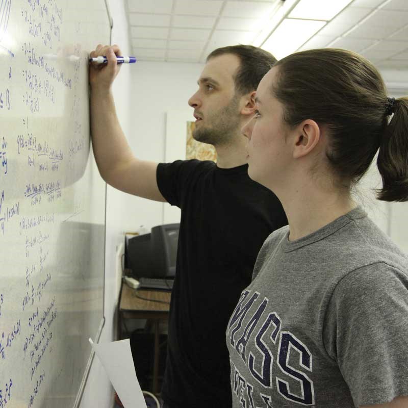 Two UMass Lowell UTeach students write equations on a whiteboard. 
