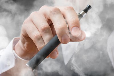 Hand holding e-cigarette surrounded by clouds of smoke.