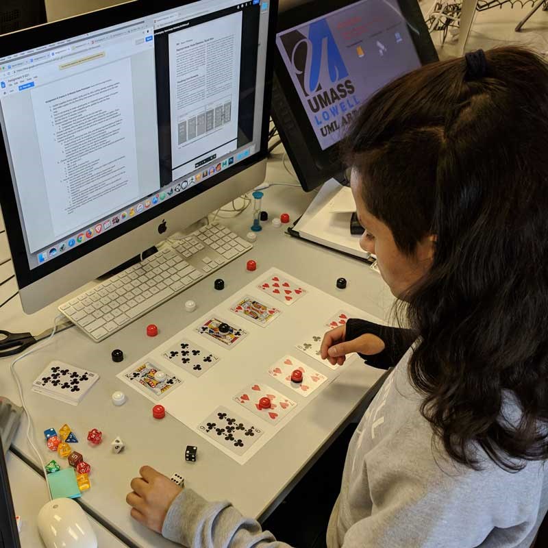 A student designs a video game using a computer, dice and cards