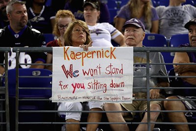 A fan sits behind a sign referring to former 49ers quarterback Colin Kaepernick 