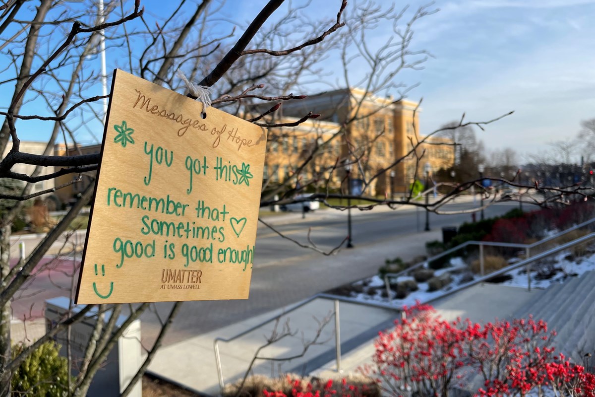 a sign of encouragement to students hangs on a tree outside on campus