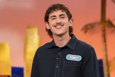 A young man with a mustache and a nametag that says Tony poses for a photo on a game show set.