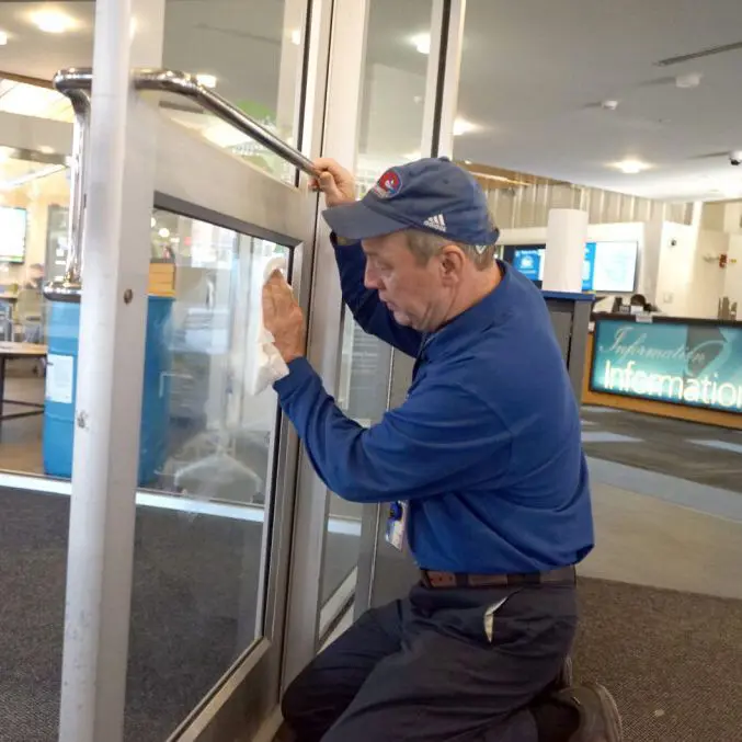 Worker wearing baseball cap wiping glass door with towel