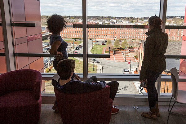 Three students looking out of a University Suites window over the city of Lowell