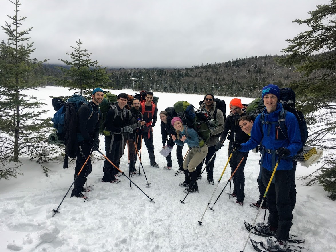Group of outdoor staff wearing backpacks in winter in snow covered forest next to frozen lake