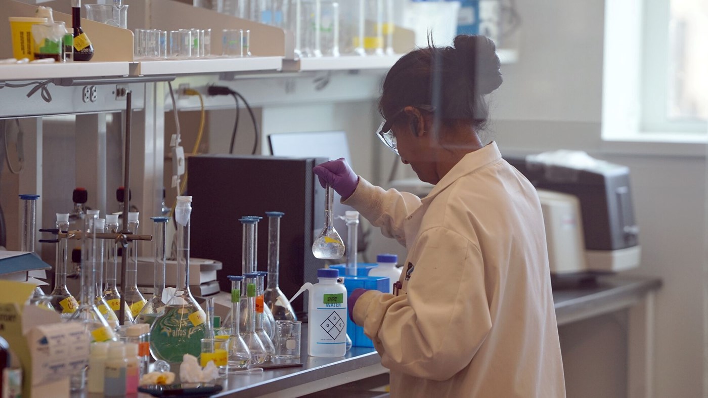 Woman in lab coat swirls liquid in a beaker