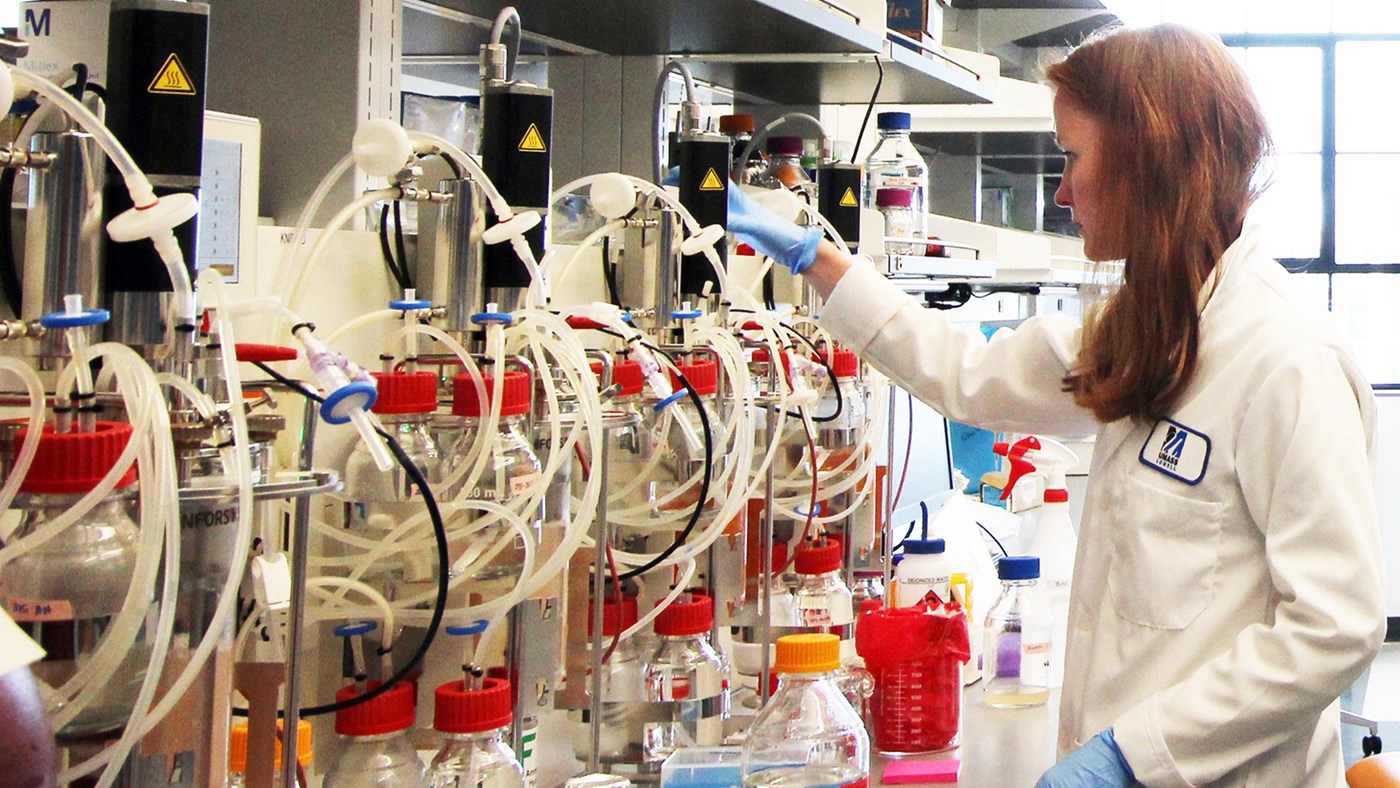 A woman in a UMass Lowell lab coat handling unknown equipment in a UMass Lowell laboratory.