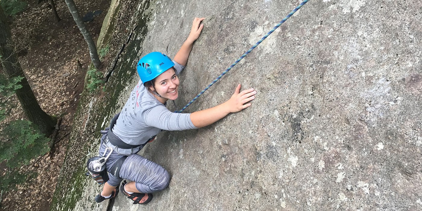 A young woman smiles while rock climbing. The Outdoor Adventure Trips program seeks to offer a variety of safe and fun outdoor trips to UMass Lowell Community. We offer trips that meet every person's skill level in order to challenge each person to grow through the experience.We encourage teamwork, skill development, personal growth and appreciation of the outdoors throughout the trip experience.