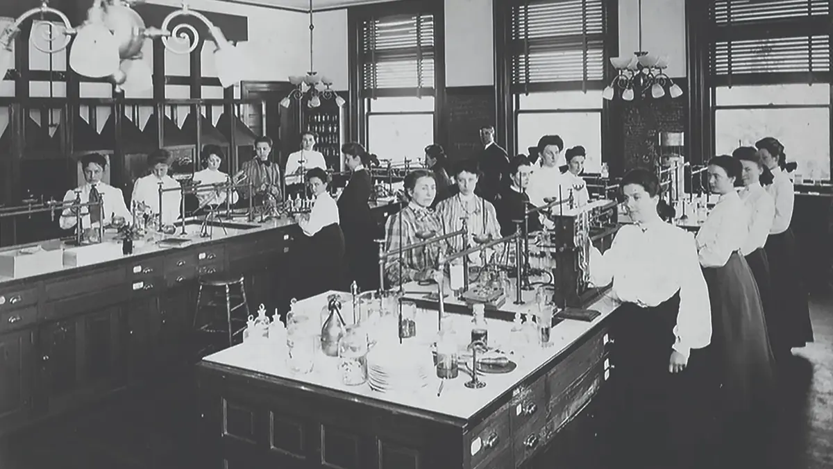 Women in high-collared blouses and long skirts work in lab