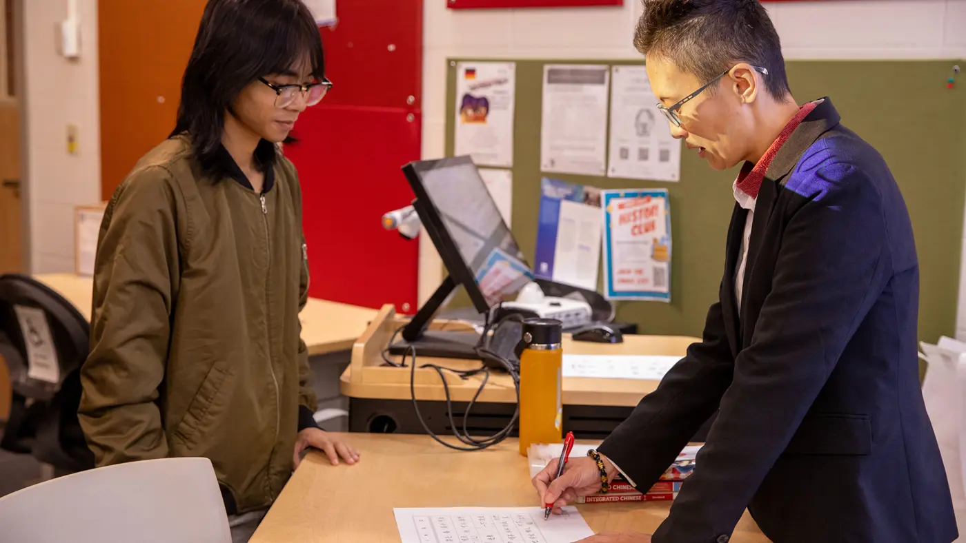 A student watches a professor write on a sheet of paper.