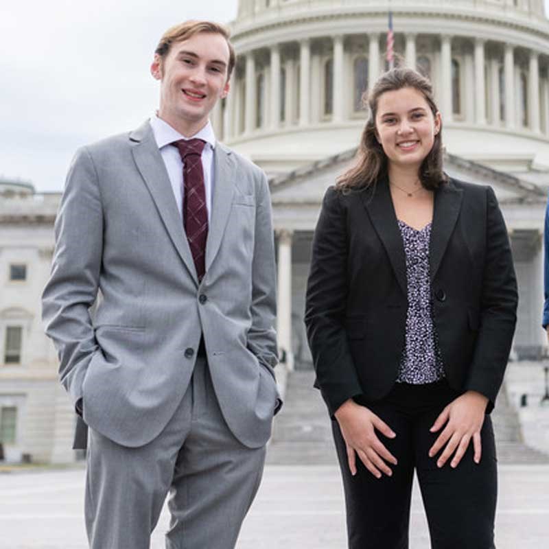 Two students wearing business attire standing in front of government building