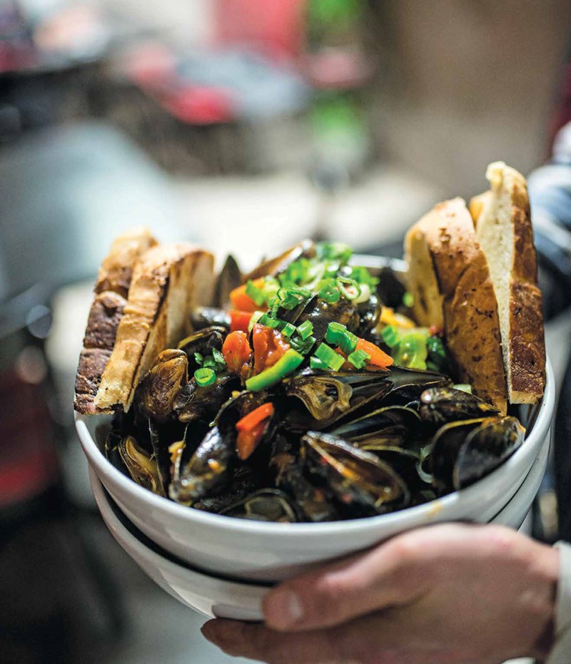 Hands holding a bowl full of mussels and 4 slices of bread from Sizzling Kitchen in Lowell