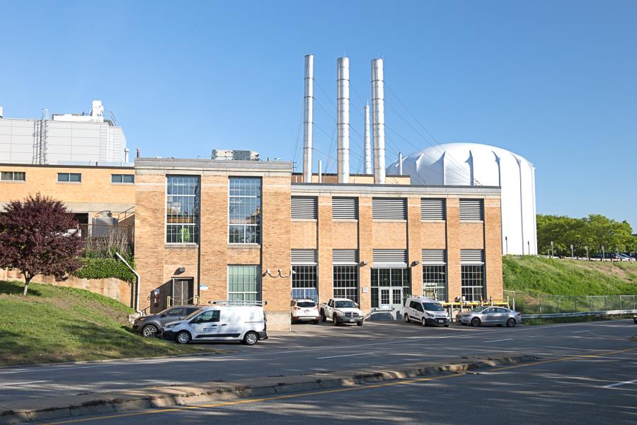 Yellow brick two-story building with trucks parked in foreground, nuclear reactor in background