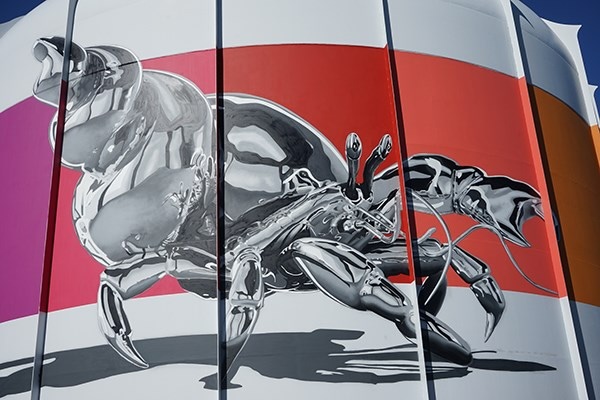 Mural of massive chrome crab with colorful bands in background