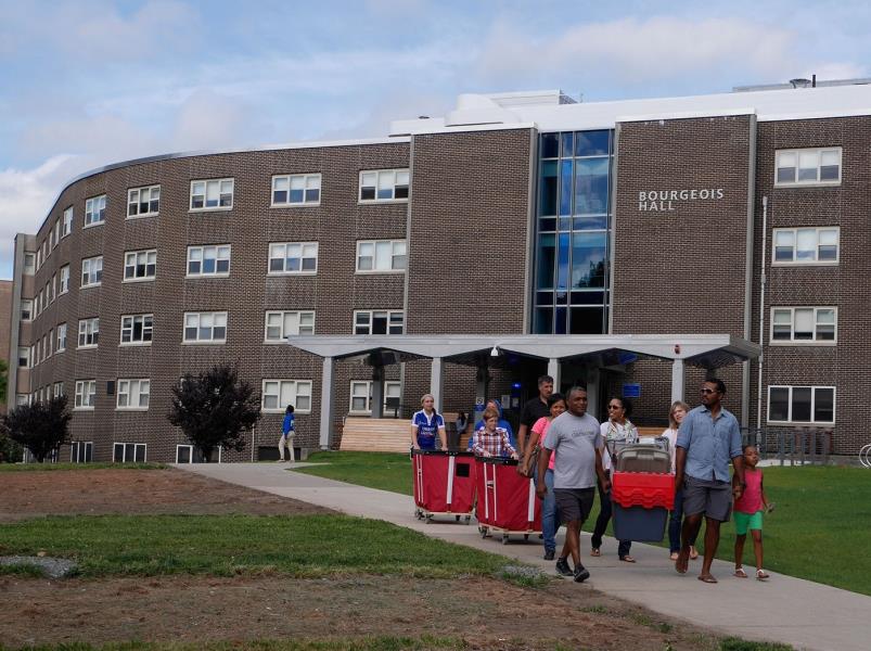 Students walk in front of Bourgeois Hall with moving bins