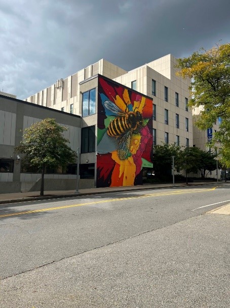 Mural of honey bee on colorful background on side of University Crossing