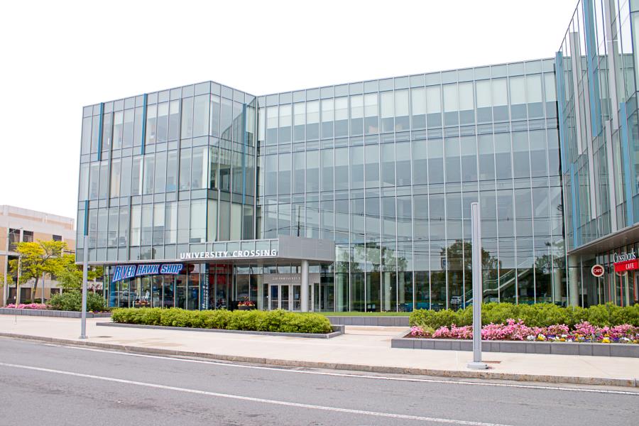 Wide shot of four-story glass paneled University Crossing building with shrubs and flowers in planters out front