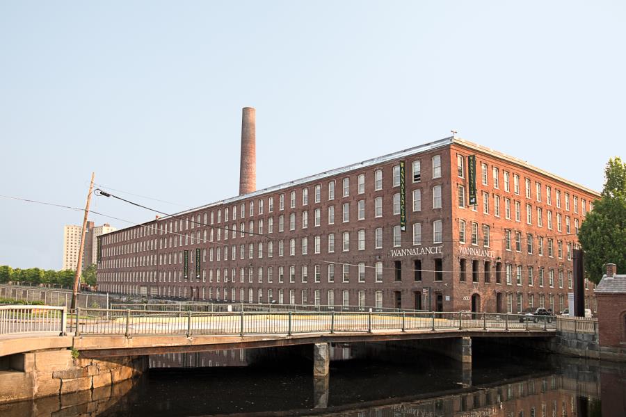 Five-story Wannalancit mill complex with smokestack atop and canal bridge in foreground