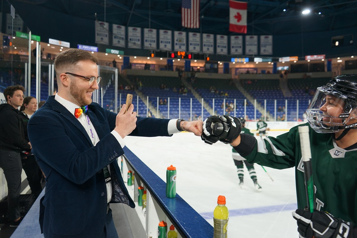 A person in a suit gives a fist bump to a hockey player who is on the ice in an arena.