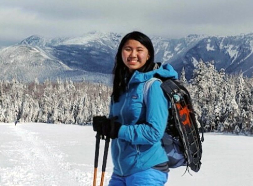 Mina Lam wearing a blue snow suit, backpack and holding poles, posing on a snowy mountain